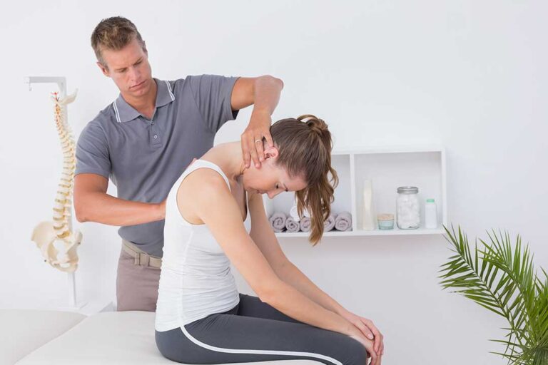 A person gently massaging their upper shoulder with one hand, showing visible muscle tension.
