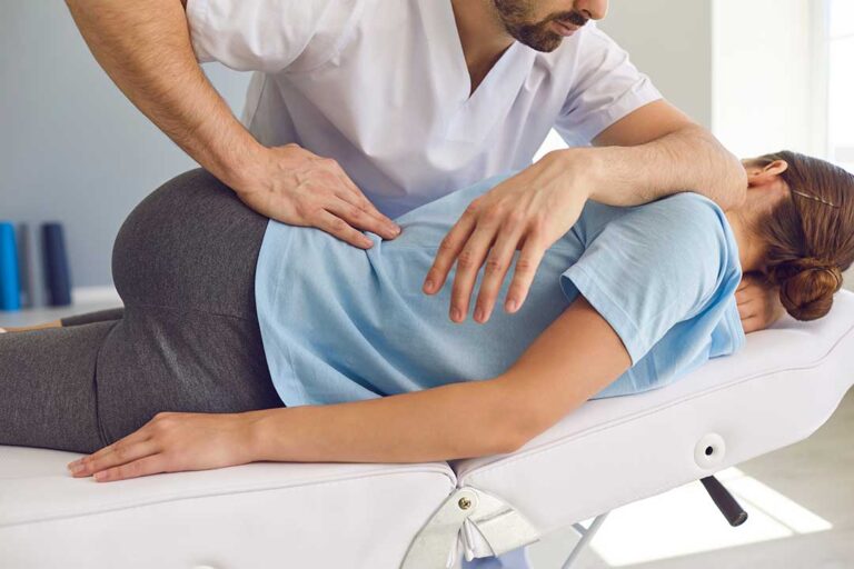A person holds an ice pack to their lower back while sitting on a living room couch.