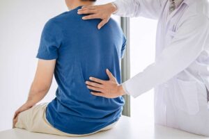 Patient discusses spinal treatment risks with a clinician beside an examination table.